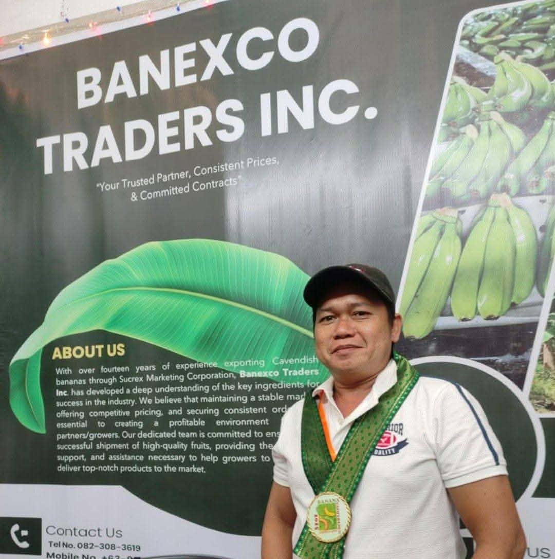 Robert Londres standing in front of a Banexco Traders Inc. banner, wearing a company medal