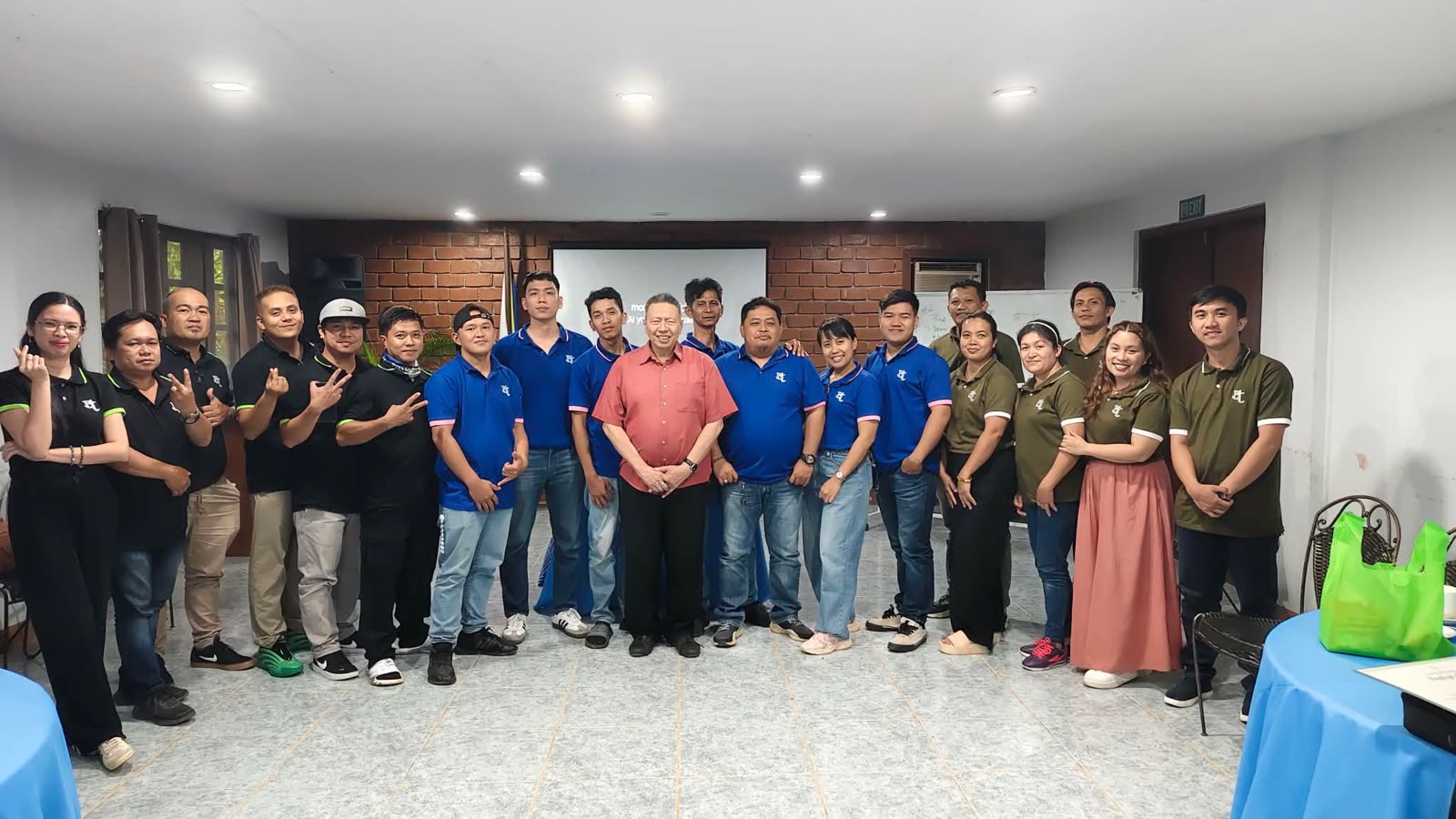 The full Banexco staff of around twenty people in company polos with the company president, gathered in an indoor hall